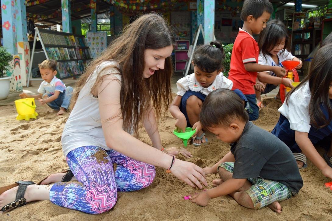 A volunteer playing with children in Cambodia A Care volunteer and children playing together in a sand pit